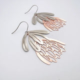 Pair of silver and rose gold leaf-shaped earrings on a light gray background