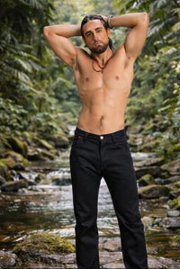 Man wearing black pants standing by a stream with greenery in the background