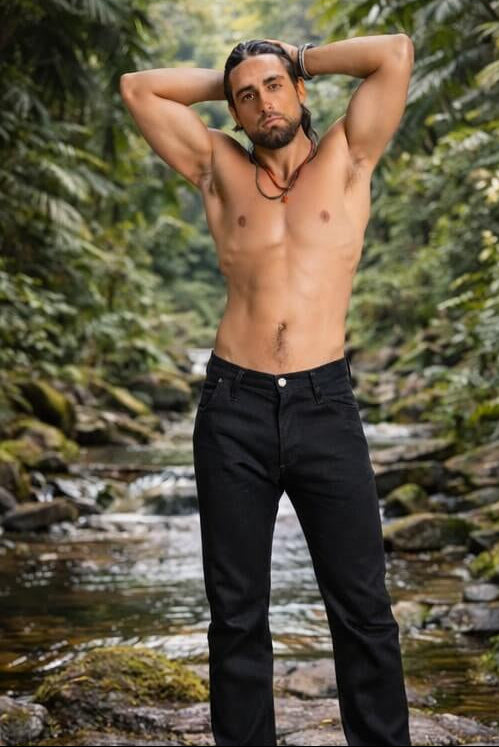 Man wearing black pants standing by a stream with greenery in the background
