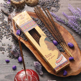 Incense sticks with packaging on a wooden tray surrounded by lavender flowers and stones.