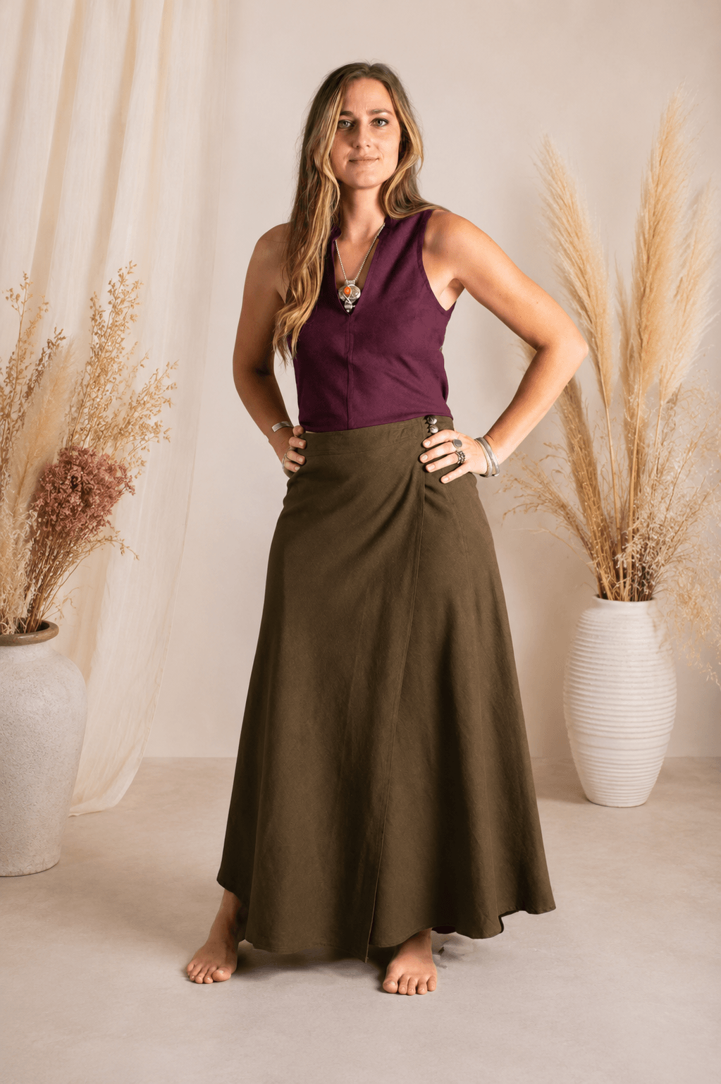 Woman wearing a purple top and brown skirt standing in front of decorative plants.