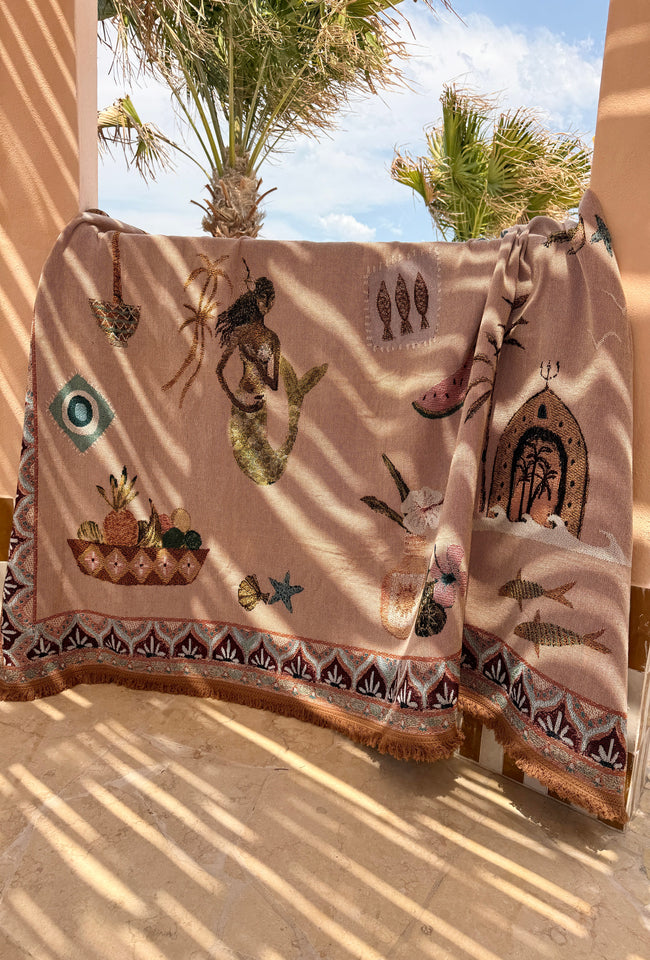 Decorative blanket with mermaid and fish designs draped over a chair outdoors.