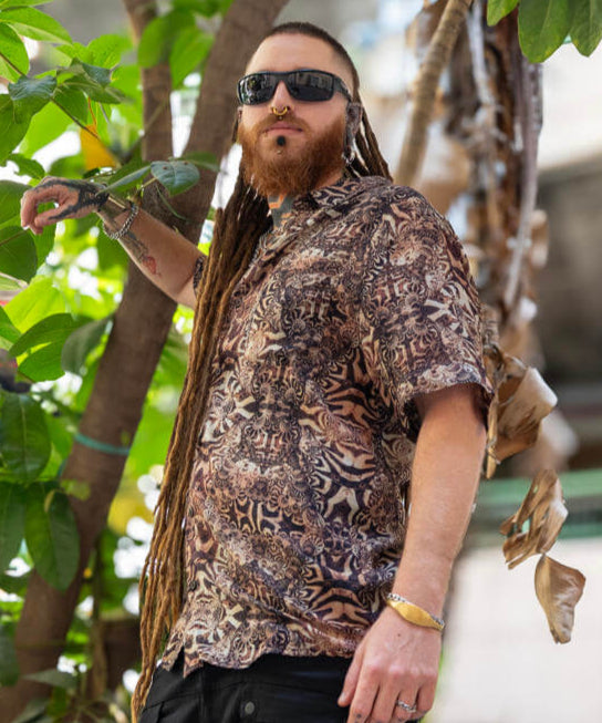 Man in a patterned shirt and black shorts standing among green foliage.