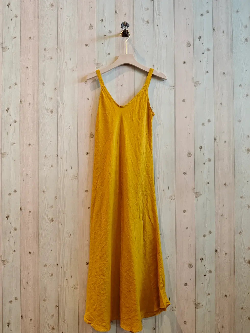 mustard colour dress on hanger against a wall
