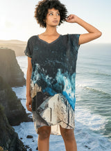 Woman wearing a patterned dress on the edge of a cliff with the ocean in the background