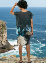 Woman wearing a patterned dress on the edge of a cliff with the ocean in the background