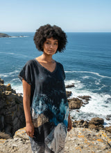 Woman wearing a patterned dress on the edge of a cliff with the ocean in the background