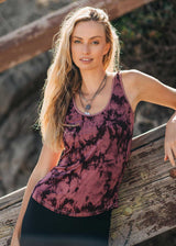 Woman wearing a purple tie-dye tank top leaning against a wooden railing.