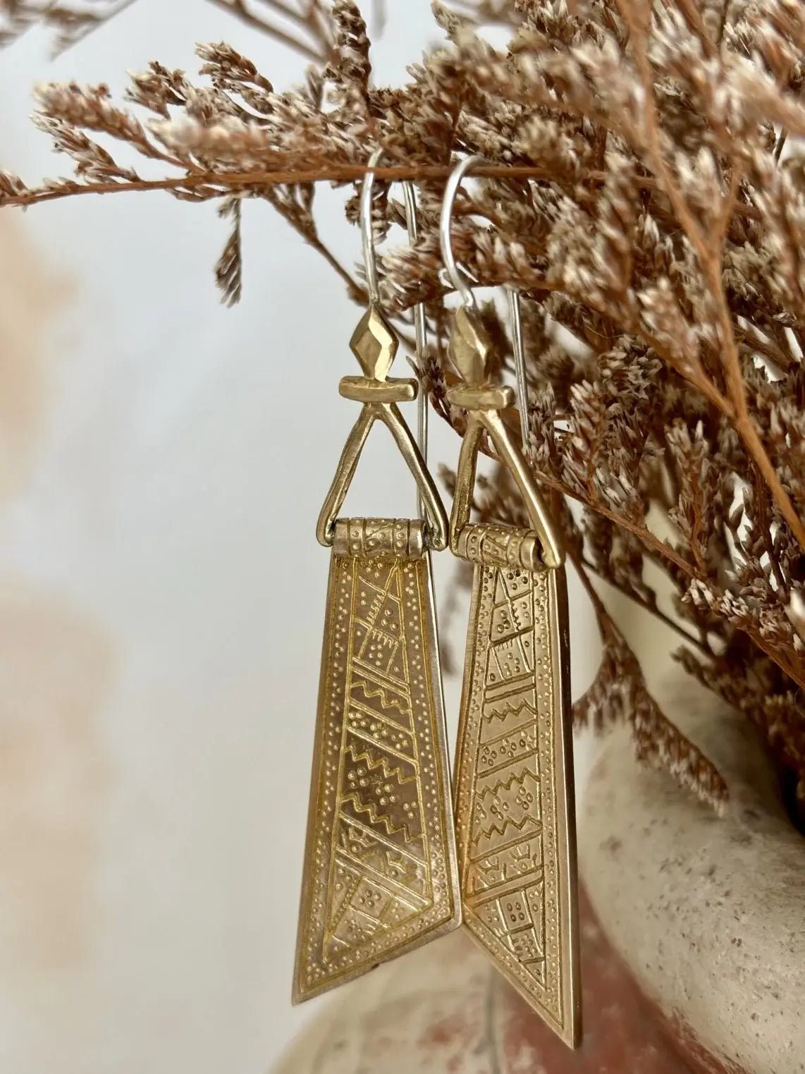 Gold earrings with intricate designs hanging on a branch.