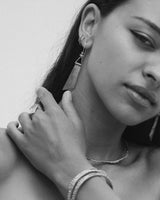 Close-up of a woman wearing earrings and a bracelet with a plain background