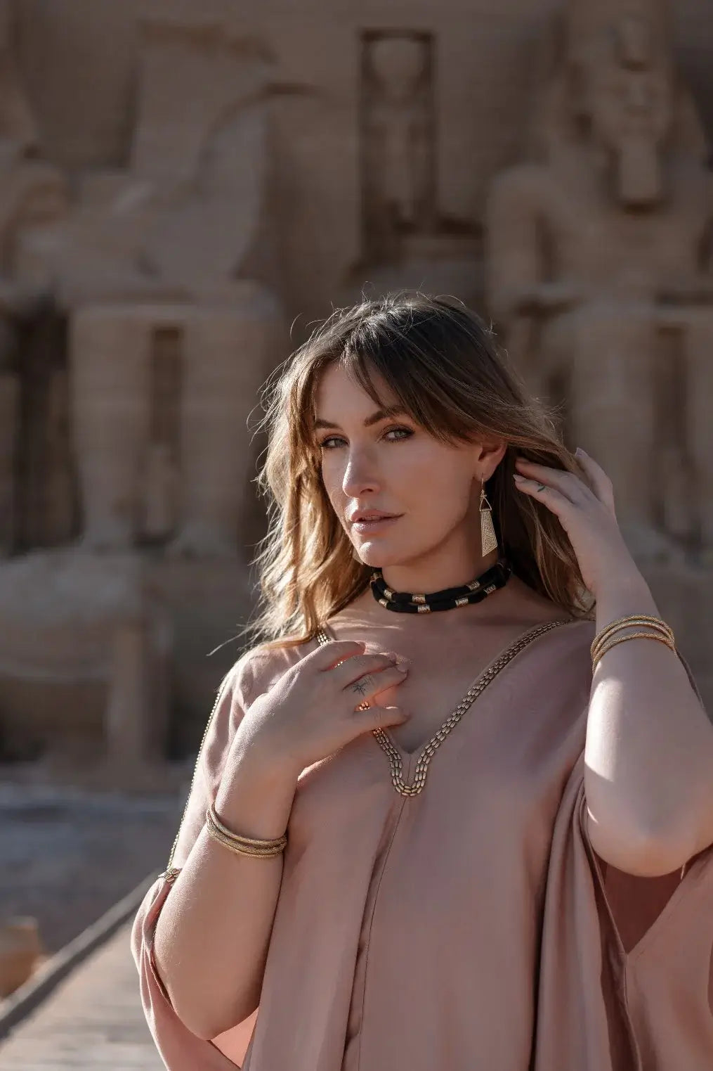 Woman in a pink dress standing in front of ancient stone statues.