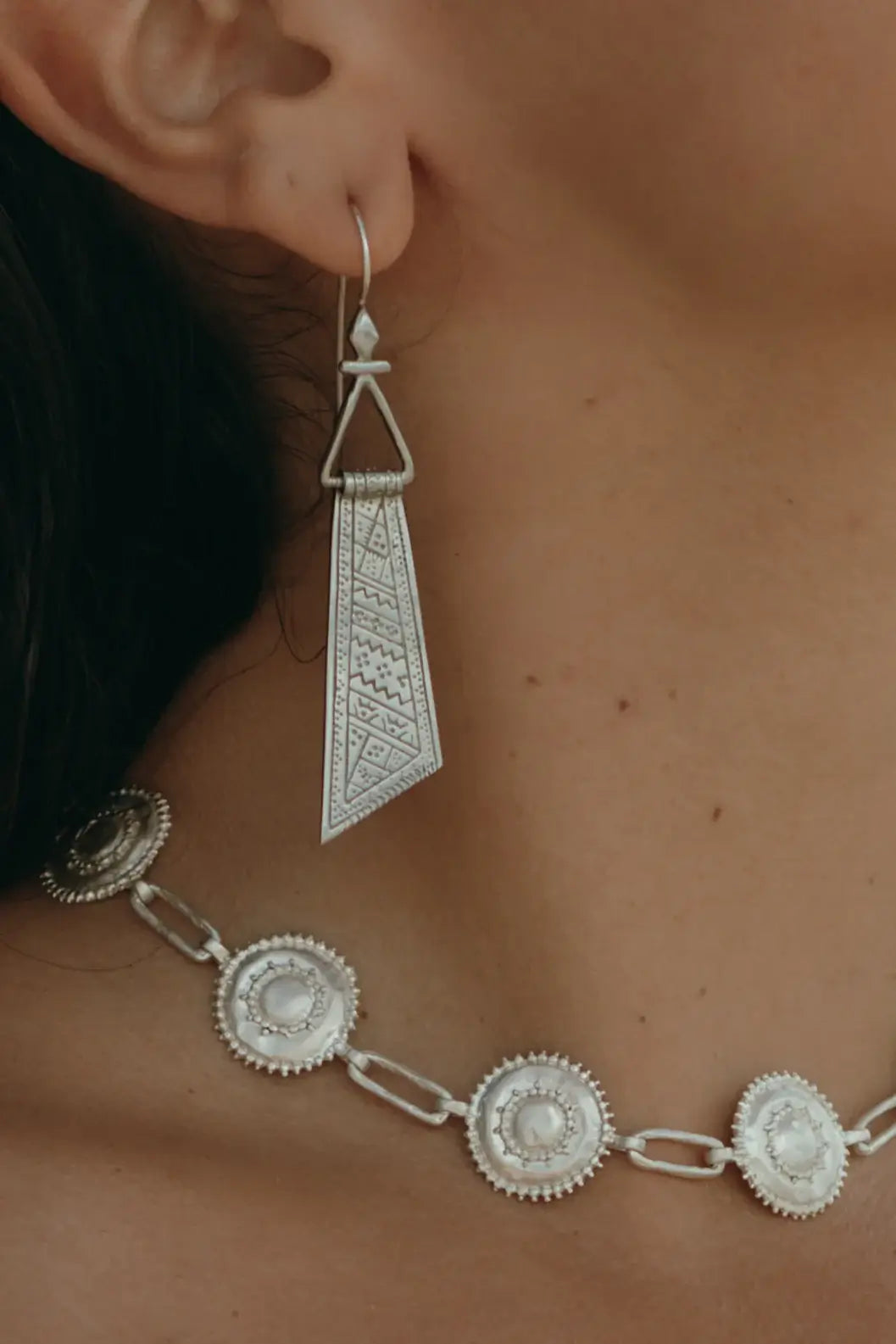Close-up of a person wearing a silver earring and necklace set.