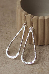 Shop Zuri Earrings in white brass with sterling silver hooks, featuring a long sculptural shape, hammered texture and lightweight feel.